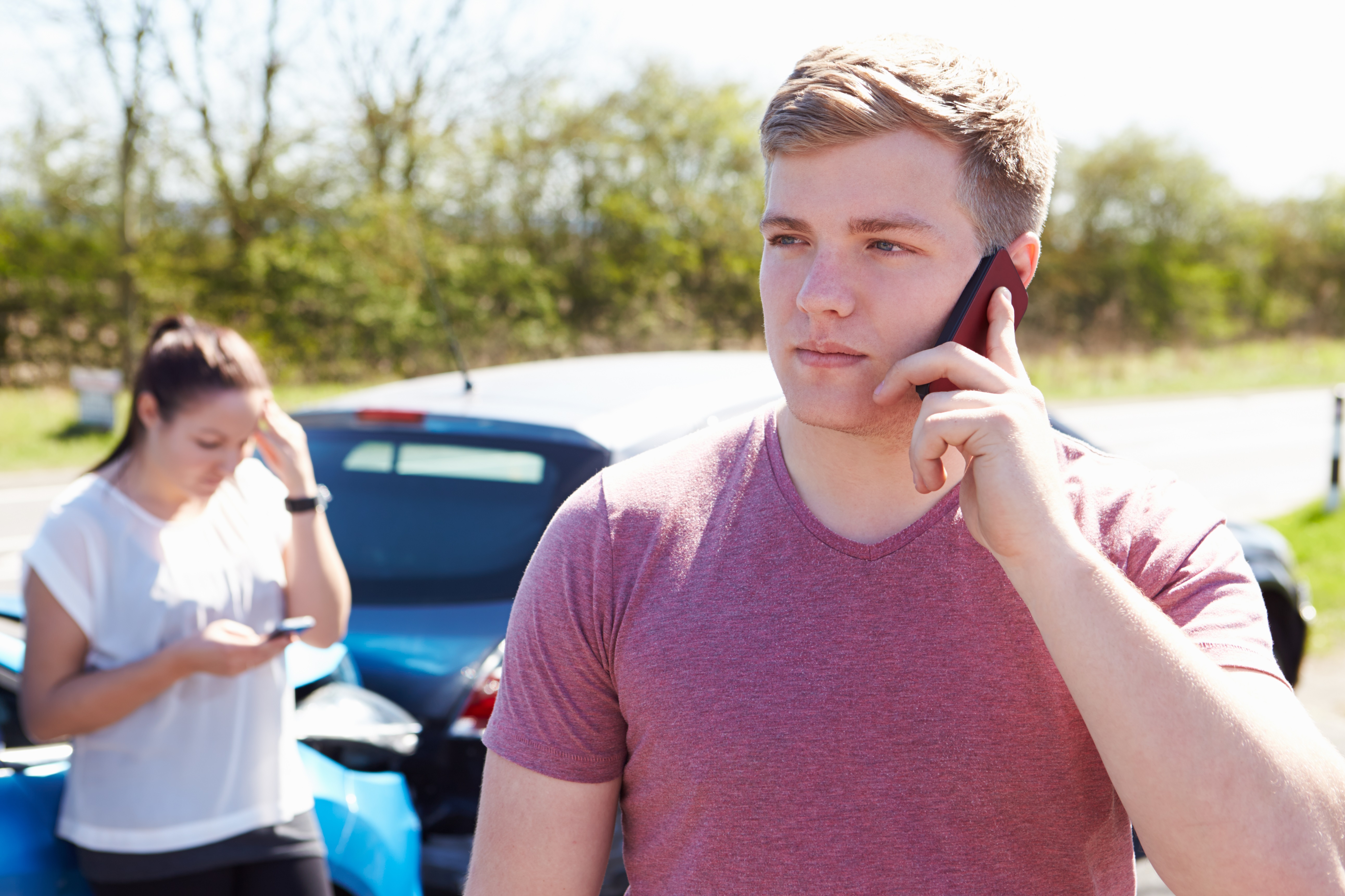 Young man makes phone call in front of car wreck
