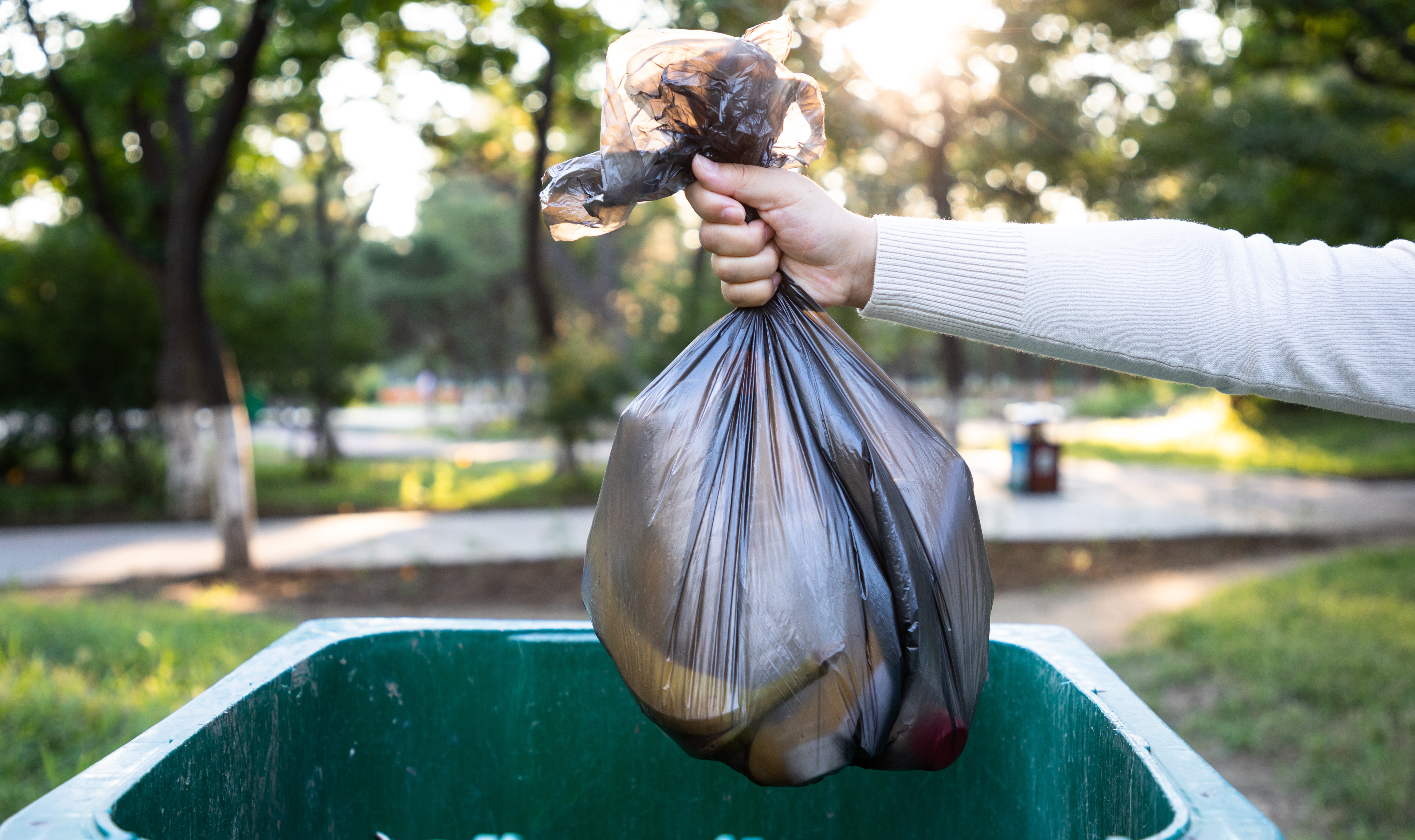 A garbage bag full of food waste hovers over a garbage bin